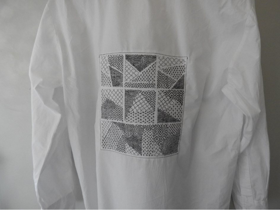 Photo d'une chemise blanche de dos avec broderie géographique apposée en technique upcycling